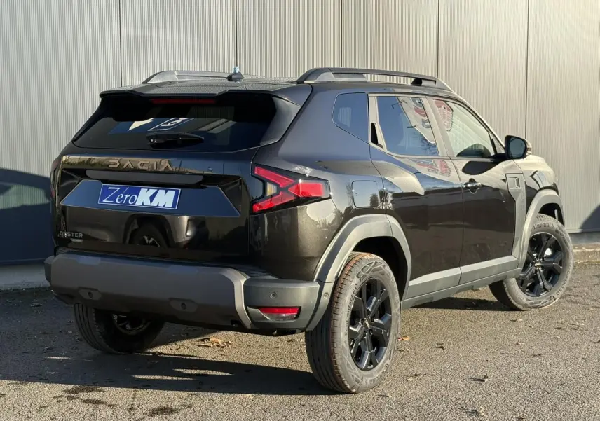 Vue 3/4 arrière droite du Dacia Duster 2026 noir nacré avec jantes alliage noires et barres de toit longitudinales.