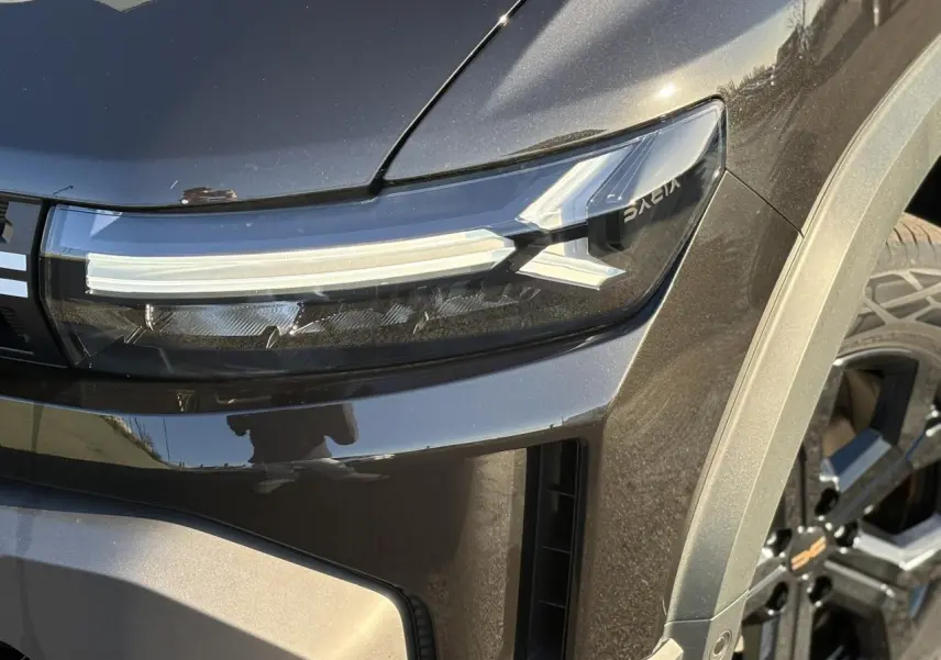 Gros plan sur le phare avant droit du Dacia Duster 2026 noir nacré avec jante alliage noire et détails modernes.