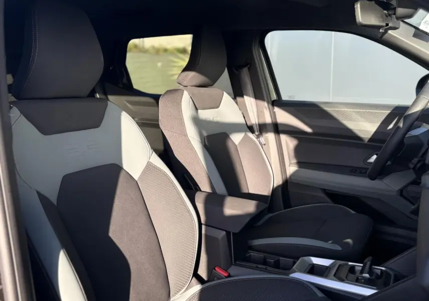 Vue intérieure côté conducteur du Dacia Duster 2026 avec sièges bi-matière gris et noir et console centrale moderne.