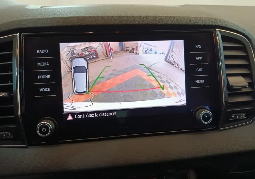 Écran tactile central montrant la caméra de recul avec vue aérienne du Skoda Karoq blanc en stationnement.
