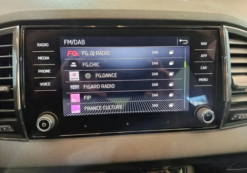 Écran tactile central du tableau de bord du Skoda Karoq blanc, affichant les stations radio FM/DAB.