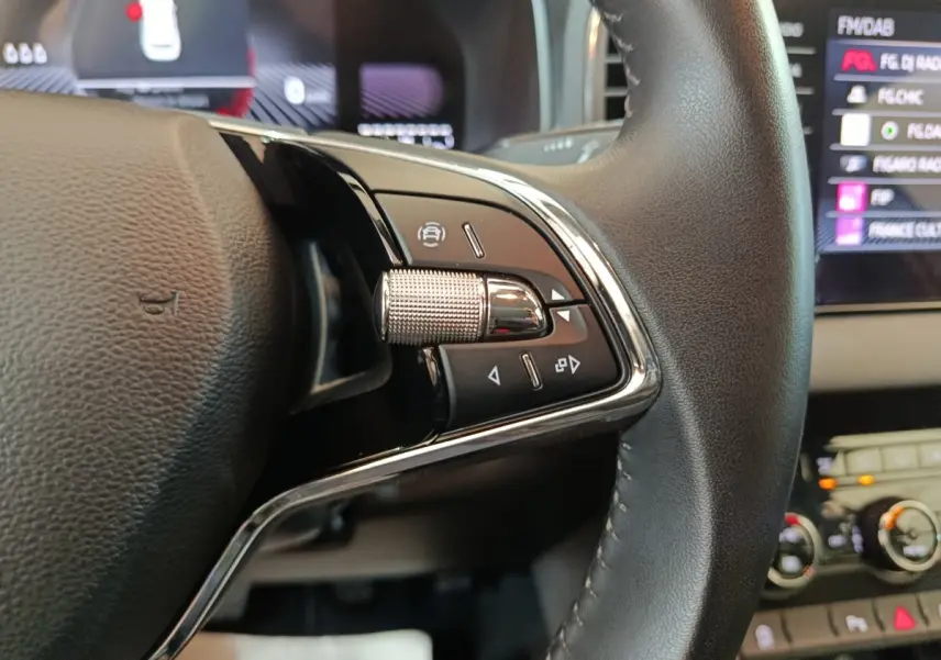 Gros plan sur les commandes multifonctions du volant cuir du Skoda Karoq blanc, avec écran tactile en arrière-plan.