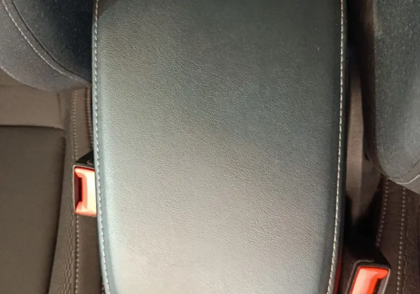 Vue rapprochée de l'accoudoir central noir en cuir et des ceintures de sécurité rouges du Skoda Karoq 2024.