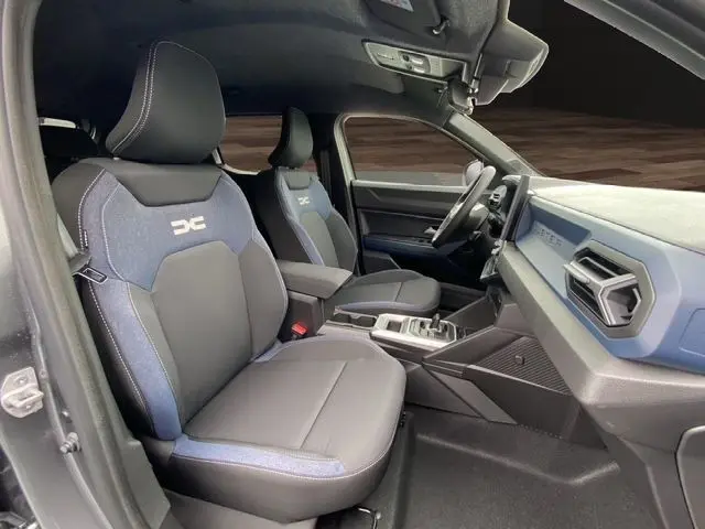 Intérieur du Dacia Duster 2025 gris schiste, vue côté gauche montrant sièges bi-matière et tableau de bord bleu.