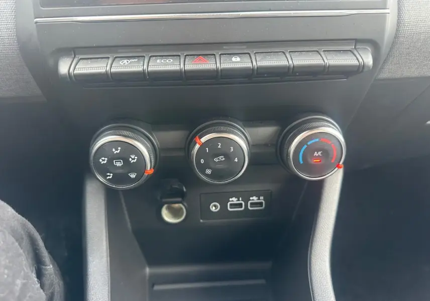 Vue rapprochée de la console centrale de la Renault Clio V dCi 100 Evolution 2025, montrant les commandes de climatisation manuelle et ports USB.