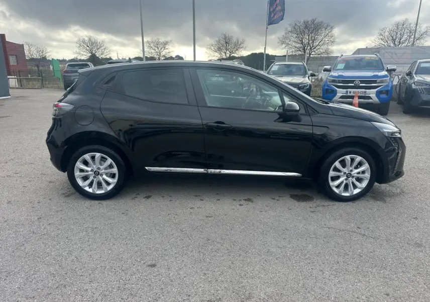 Profil droit d'une Renault Clio V dCi 100 Evolution noire 2025 avec vitres surteintées et jantes argentées, stationnée en extérieur.
