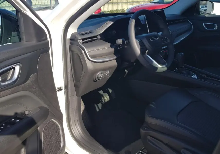 Intérieur côté conducteur du Jeep Compass blanc 2024, avec tableau de bord et volant visibles, porte ouverte.