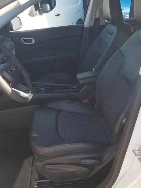 Vue intérieure côté conducteur du Jeep Compass blanc 2024, sièges noirs avec accoudoir central et commandes visibles.