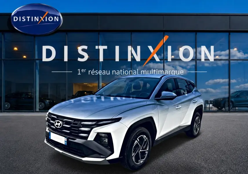 Hyundai Tucson blanc en 3/4 avant droit, avec calandre noire et jantes alliage distinctives devant showroom Distinxion.