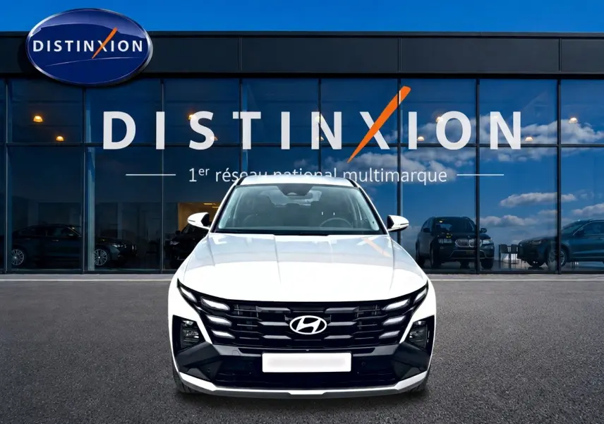 Vue de face du Hyundai Tucson blanc 2026 avec calandre noire distinctive devant une vitrine Distinxion.
