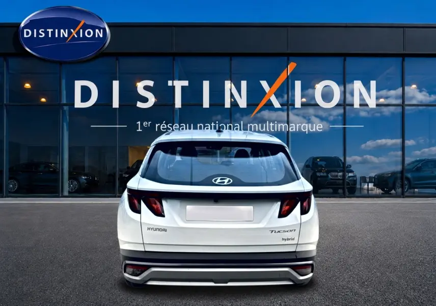 Vue arrière d'un Hyundai Tucson blanc hybride 2026 stationné devant une vitrine avec logo Distinxion.