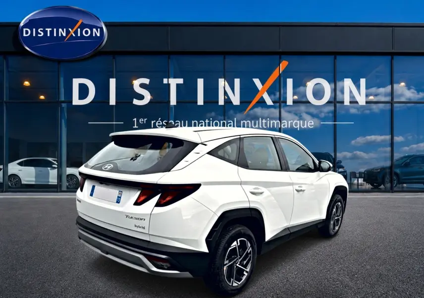 Vue 3/4 arrière droite d'un Hyundai Tucson blanc hybride devant une vitrine avec logo Distinxion.