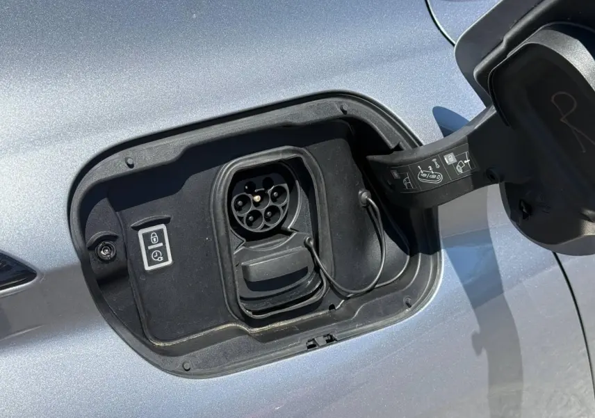 Prise de recharge électrique ouverte en gros plan sur le côté gauche d’une Peugeot 308 e-308 gris Artense.