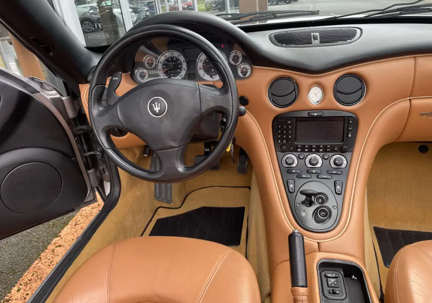 Intérieur cuir beige de la Maserati Spyder 2002, vue du poste de conduite avec volant trident et console centrale élégante.