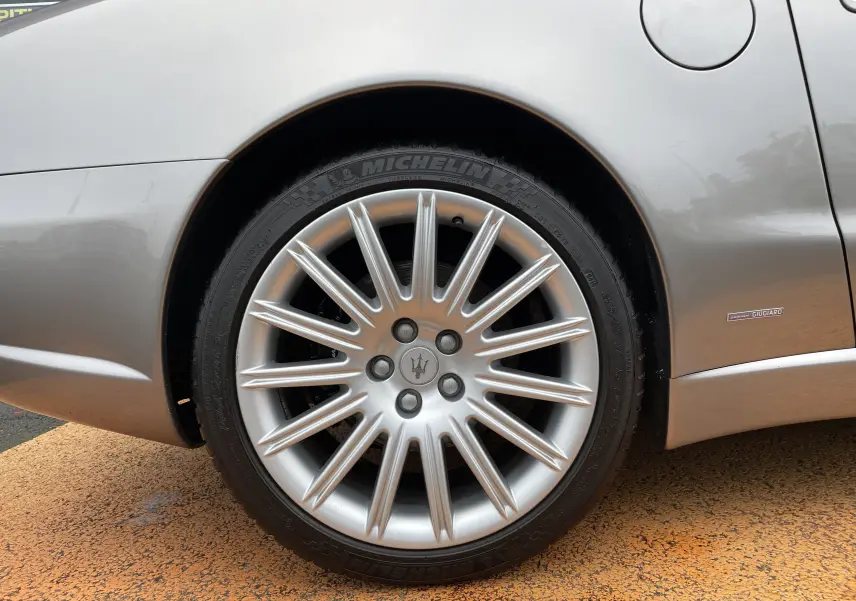 Gros plan sur la roue arrière droite gris Nuvolari d'une Maserati Spyder 2002 avec jante étoilée et badge Giugiaro.