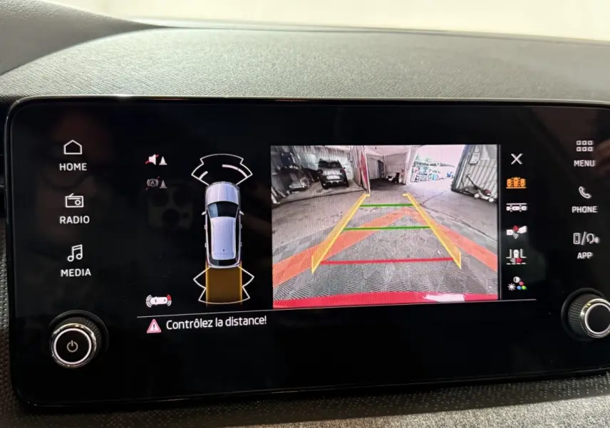 Écran tactile central du Skoda Kamiq rouge 2024 montrant la caméra de recul et les capteurs de stationnement.