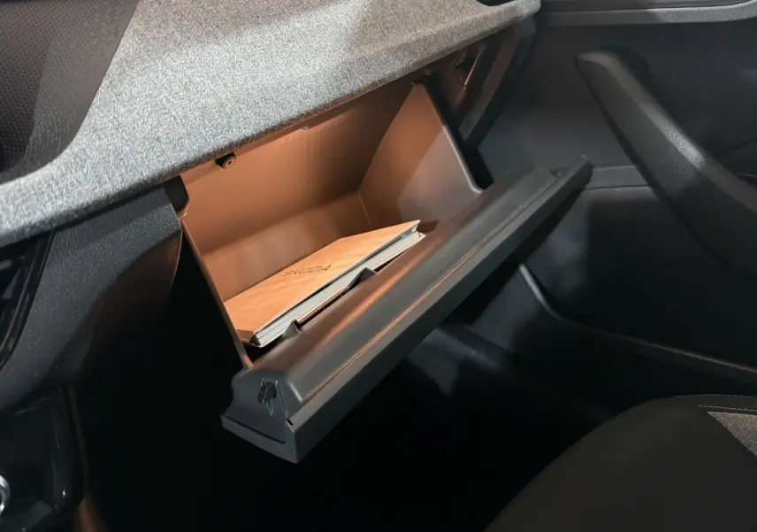 Gros plan sur la boîte à gants ouverte du Skoda Kamiq 2024, montrant un manuel à l'intérieur, intérieur noir.