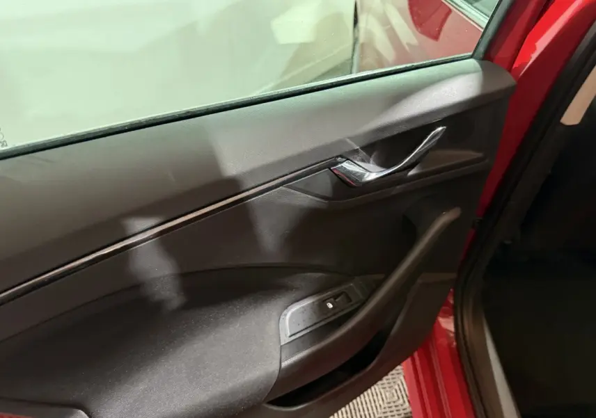 Gros plan sur la porte côté gauche intérieure noire avec poignée chromée d'un Skoda Kamiq rouge 2024.