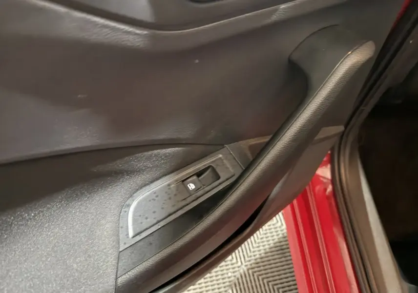 Poignée de porte intérieure noire côté conducteur sur SKODA KAMIQ rouge, avec bouton de verrouillage des vitres.