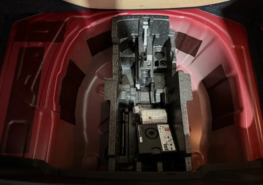 Coffre ouvert du Skoda Kamiq rouge 2024, montrant le rangement sous tablette avec kit de réparation pneus.