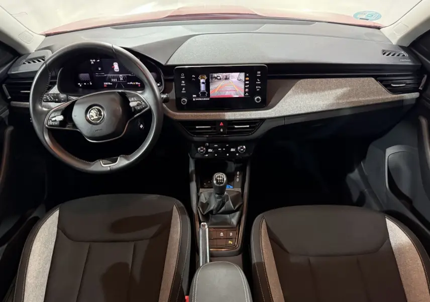 Vue intérieure frontale du tableau de bord et volant cuir noir du Skoda Kamiq 2024 avec écran tactile et levier de vitesses manuel.