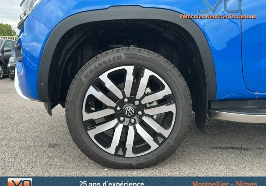 Gros plan sur la roue avant droite du Volkswagen Amarok bleu 2025 avec jante alliage 21 pouces et marchepied visible.