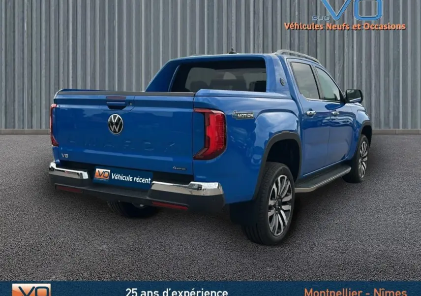 Vue 3/4 arrière droite d'un Volkswagen Amarok bleu avec jantes alliage 21 pouces et marchepieds visibles.