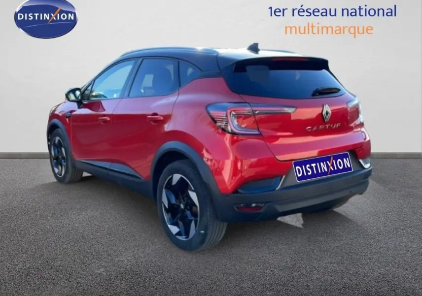 Vue 3/4 arrière droite d'un Renault Captur rouge 2025 avec jantes aluminium et barres de toit visibles.