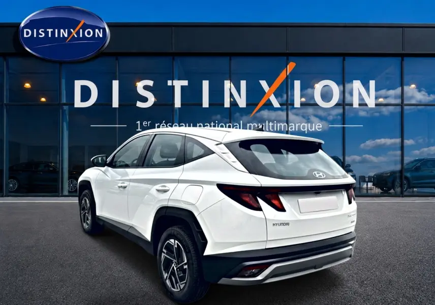 Vue 3/4 arrière droite d’un Hyundai Tucson blanc 2026 devant une vitrine avec logo Distinxion.