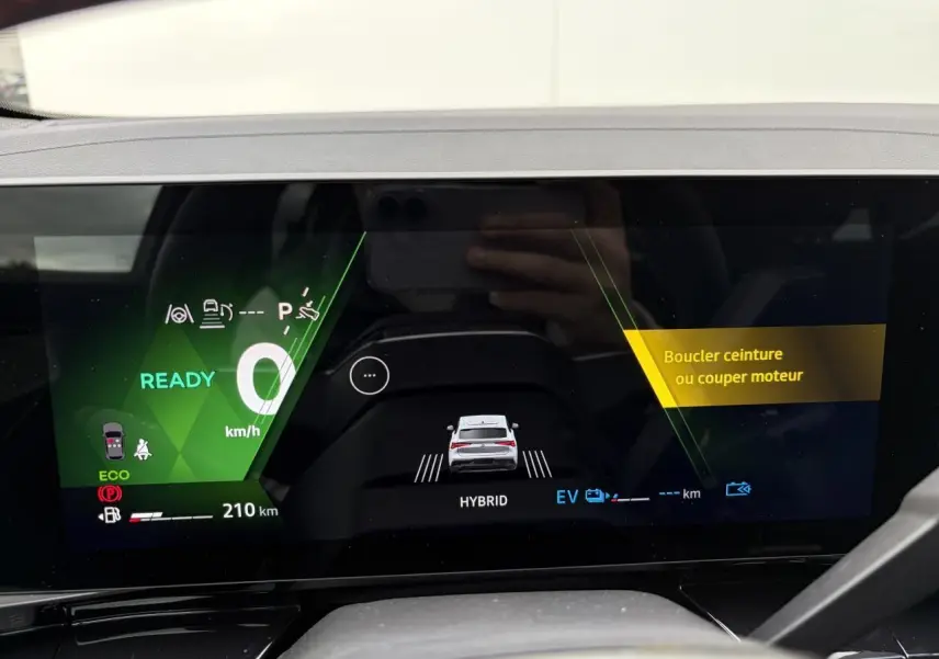 Écran numérique du tableau de bord montrant la Renault Rafale hybride en vue arrière stylisée avec alertes de sécurité affichées.