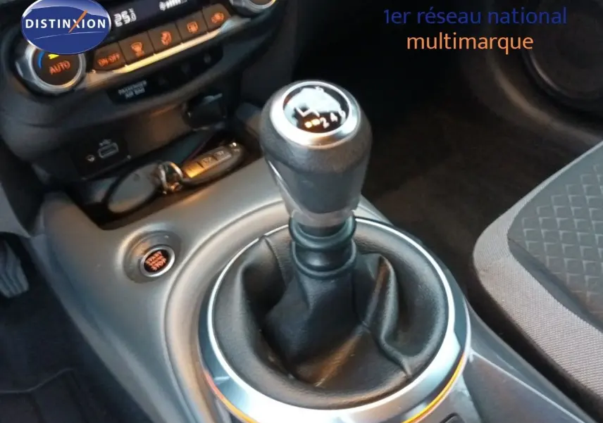 Gros plan sur le levier de vitesses manuel du Nissan Juke gris platine, avec console centrale et commandes climatiques visibles.