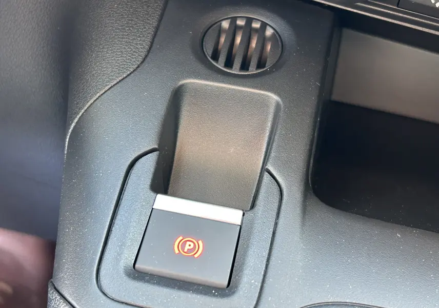 Gros plan sur le bouton de frein à main électrique rouge dans l'habitacle noir du Peugeot Partner Dangel gris Artense.