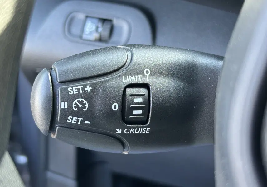 Gros plan sur la commande de régulateur et limiteur de vitesse du DANGEL Peugeot Partner gris Artense, côté gauche du volant.