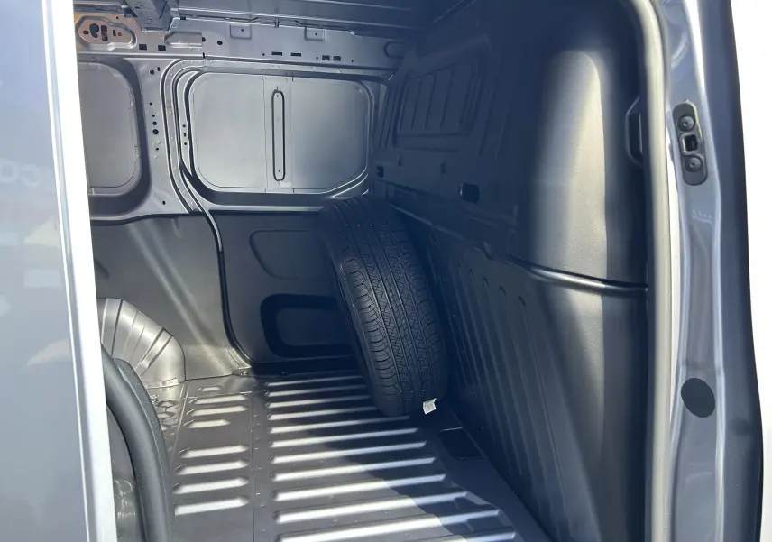 Vue intérieure de la zone de chargement du Peugeot Partner Dangel gris Artense avec une roue de secours appuyée sur la paroi.