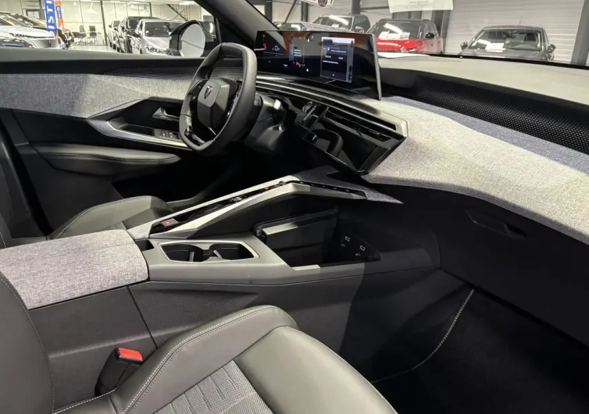 Vue intérieure côté conducteur du Peugeot 3008 2025, avec tableau de bord tissu gris clair et écran panoramique flottant.