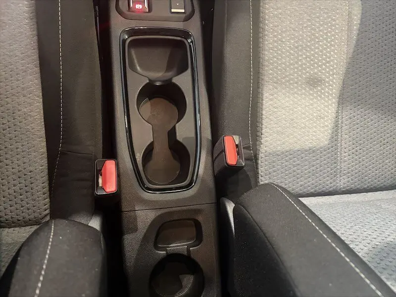 Vue plongeante sur la console centrale noire de l’Opel Corsa gris 2025, avec porte-gobelets et ceintures rouges visibles.