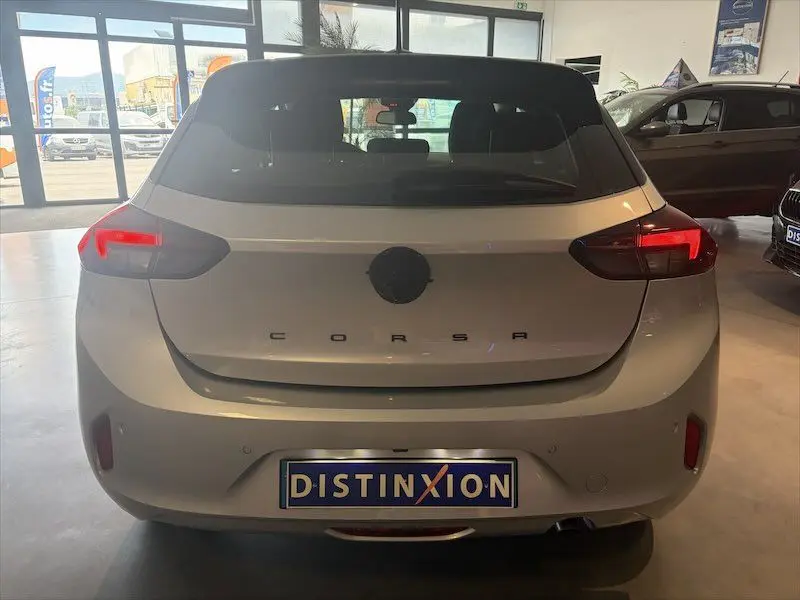 Vue arrière d'une Opel Corsa gris clair 2025 en concession, avec feux arrière allumés et logo masqué.