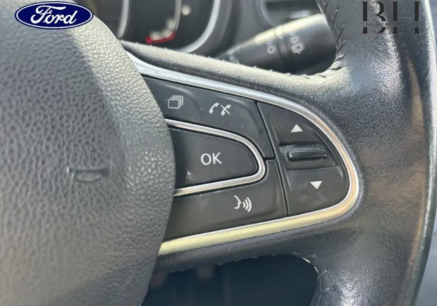 Gros plan sur les commandes au volant en cuir noir d’un véhicule, avec boutons multifonctions visibles.
