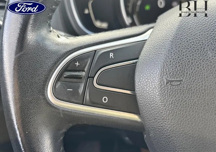 Gros plan sur les commandes du volant en cuir noir d’un véhicule, avec boutons de réglage du régulateur de vitesse.