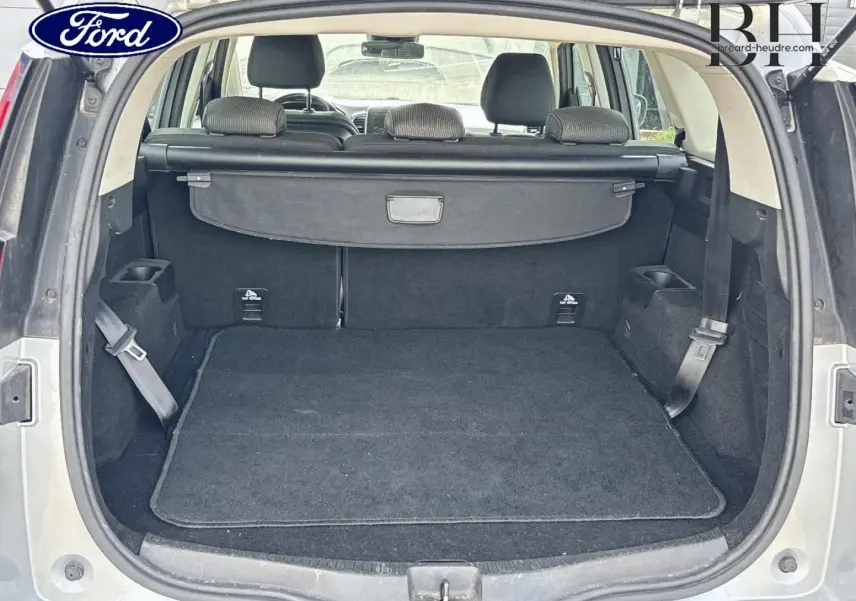 Coffre ouvert vu de l'arrière d'un Renault Grand Scenic gris platine avec cache-bagages et sièges arrière visibles.