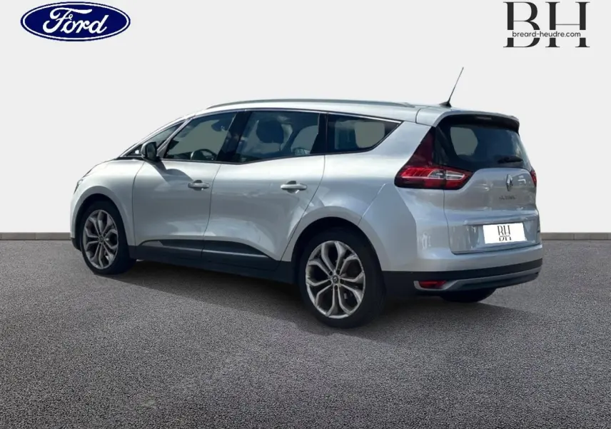 Vue 3/4 arrière droite d'un Renault Grand Scenic gris platine avec vitres teintées et barres de toit visibles.