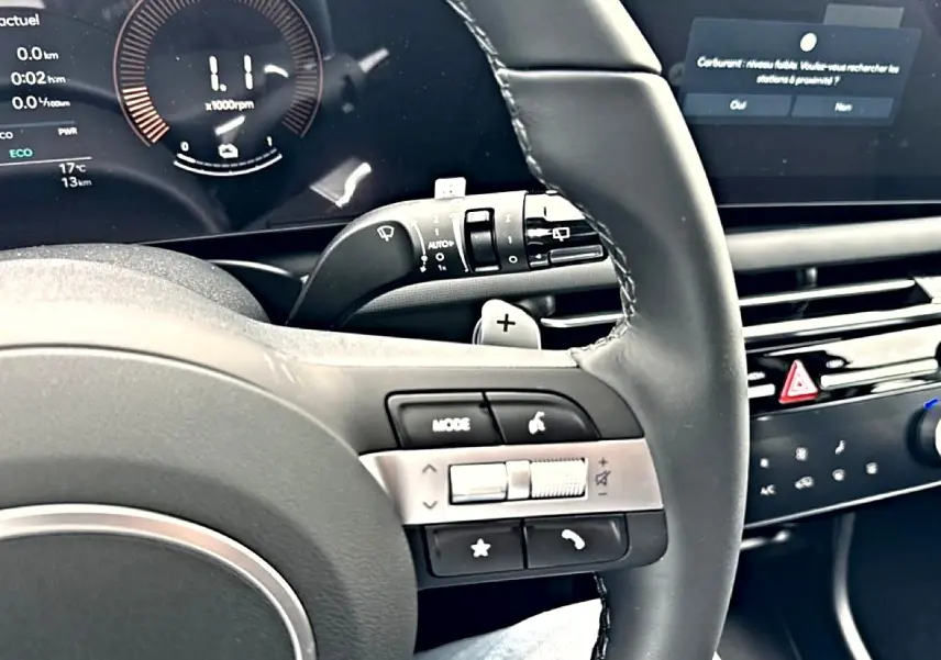 Vue rapprochée du volant cuir multifonction noir du Hyundai Tucson 2026 avec commandes audio et écran digital en arrière-plan.