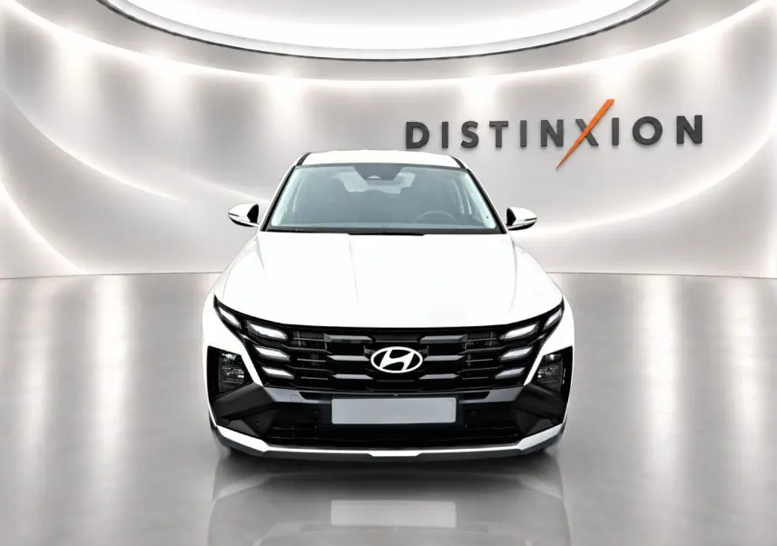 Vue frontale du Hyundai Tucson blanc 2026 avec calandre noire et éclairage LED distinctif en showroom.