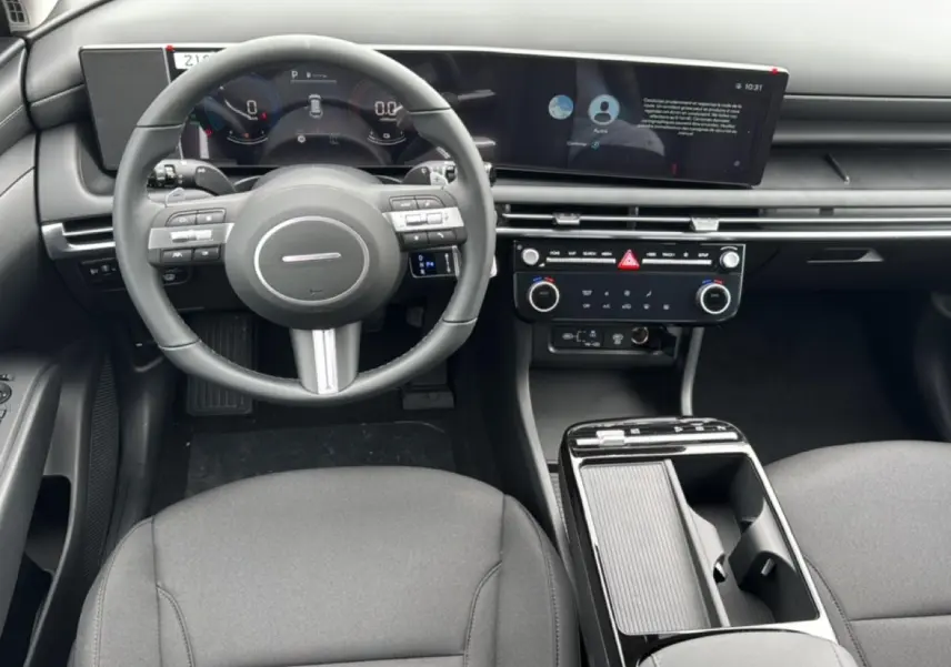Vue intérieure avant du Hyundai Tucson 2026 hybride, montrant le volant multifonction, l'écran large et la console centrale noire.