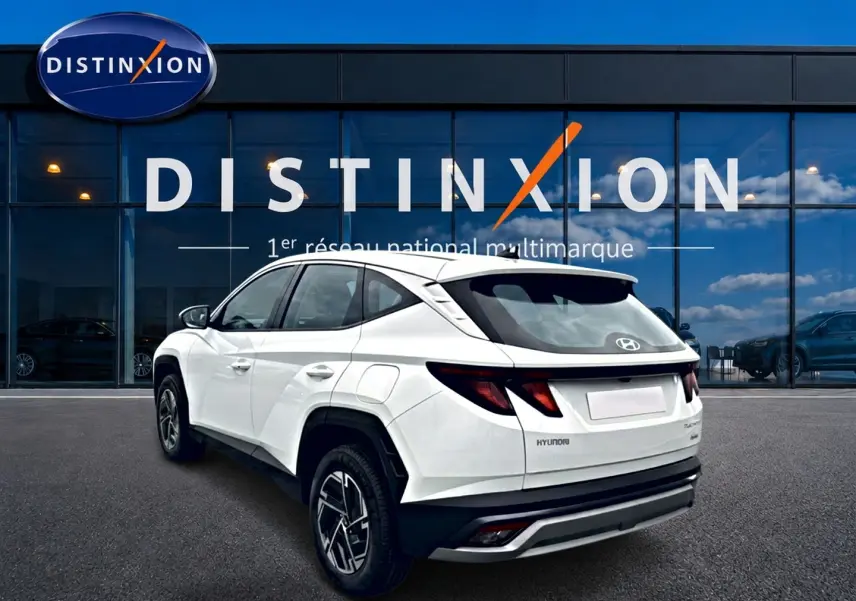 Vue 3/4 arrière gauche du Hyundai Tucson blanc 2026 avec jantes alliage et feux arrière LED, devant une vitrine Distinxion.
