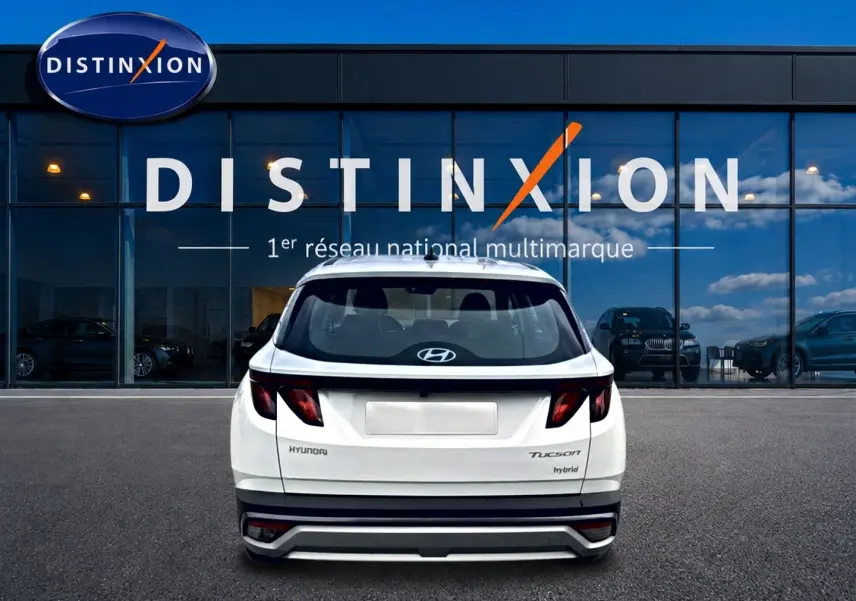 Vue arrière d'un Hyundai Tucson blanc hybride garé devant une vitrine avec logo Distinxion.