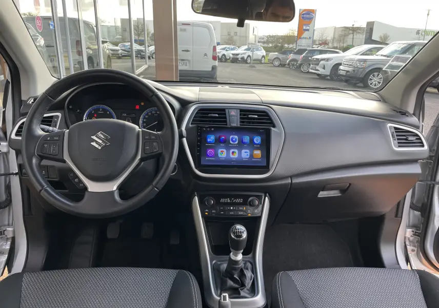 Vue intérieure avant du Suzuki SX4 S-Cross 2016 gris, avec tableau de bord moderne et écran tactile central.