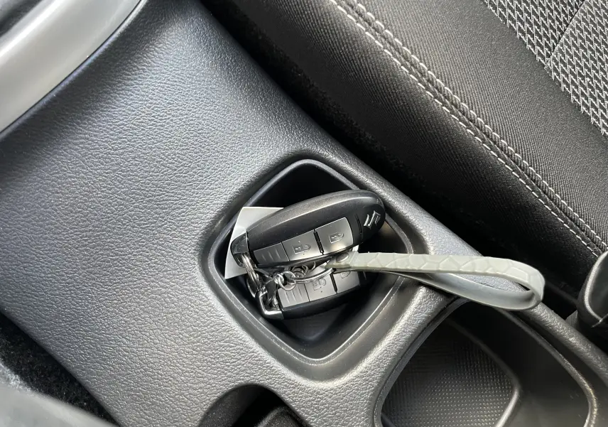 Gros plan sur la clé de contact Suzuki posée dans le rangement central noir à côté du siège tissu gris.