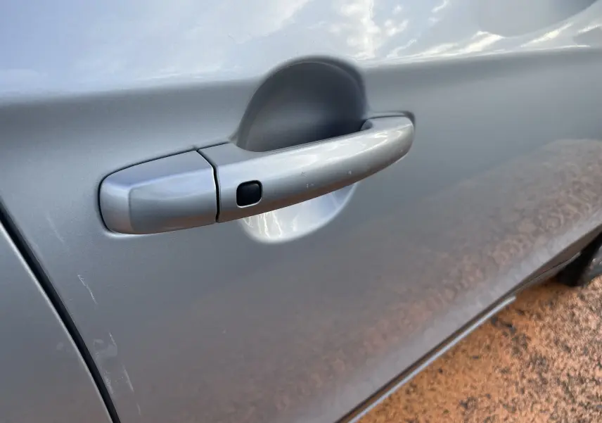 Poignée de porte côté gauche gris métallisé du Suzuki SX4 S-CROSS 2016 avec bouton de déverrouillage sans clé visible.