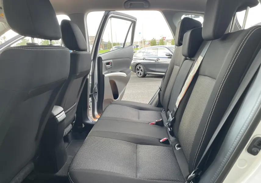 Vue intérieure arrière gauche sur la banquette noire du Suzuki SX4 S-CROSS 2016 avec porte ouverte et voiture grise en arrière-plan.